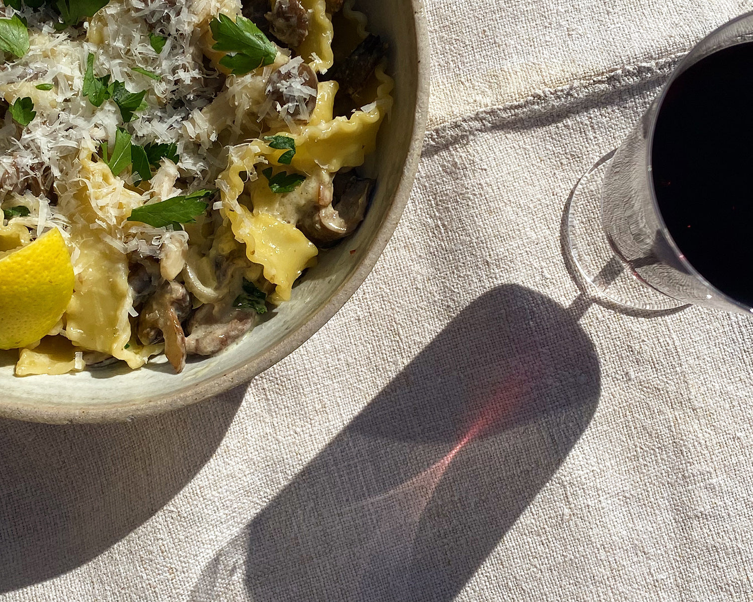 Close up of a bowl filled with creamy mushroom pasta next to a glass of Avaline Red