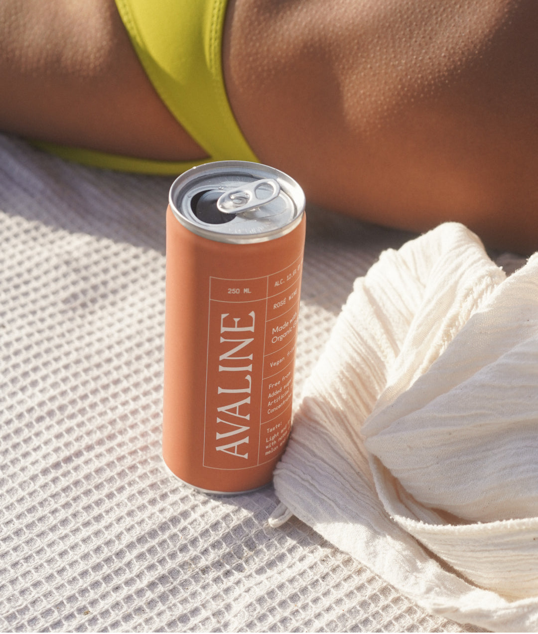 Avaline Rosé can sitting on a beach blanket next to a woman sunbathing
