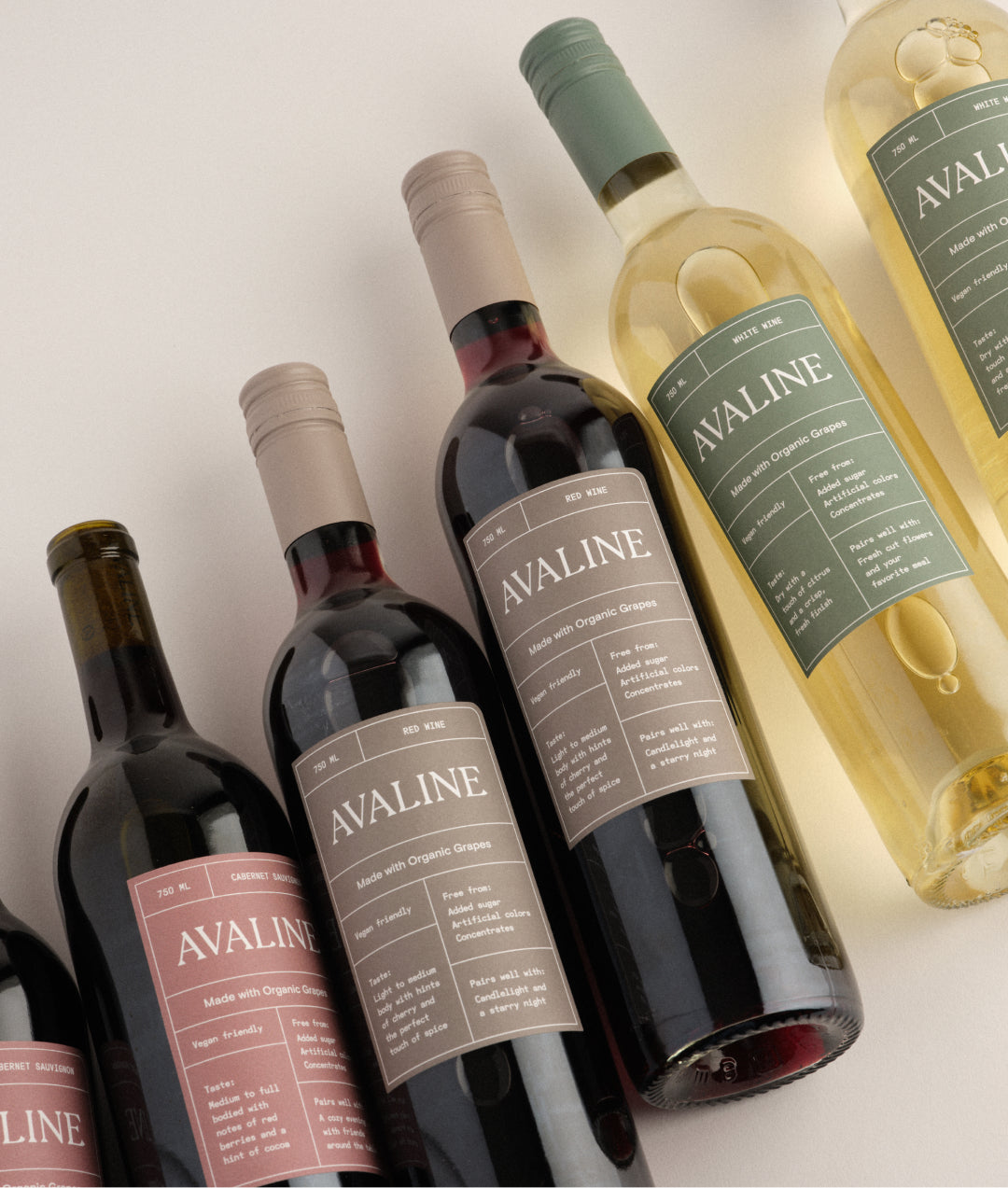 A lineup of wine bottles lying down on a table featuring Avaline White, Red, and Cabernet Sauvignon against a white background.